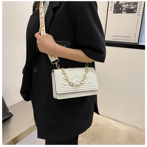 Detailed view of white quilted crossbody bag with gold chain and embroidered strap