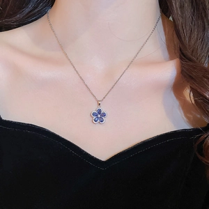 Close-up of a silver necklace featuring a delicate five-petal blue flower pendant with crystals