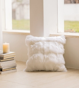 Close-up of a white plush square cushion on a wooden floor with cozy home lighting