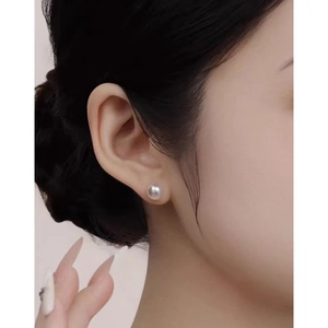 Close-up of a round cream white pearl earring with soft iridescent luster on model