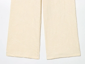 Détail de la broderie florale 3D sur l'ourlet du pantalon blanc cassé avec texture de qualité