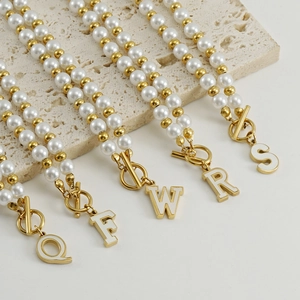 Gros plan de pendentifs lettres Q, F, W, R, S en or 18 carats avec perles sur base en pierre