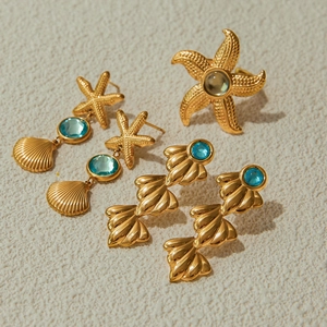 Detail shot of gold starfish and shell jewelry set with blue gems on beige surface