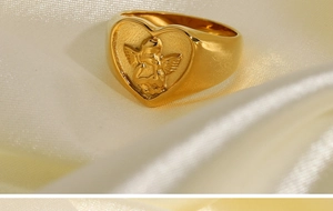 Macro shot of gold-plated angel heart ring resting on elegant beige silk fabric