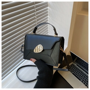 Detail of minimalist black crossbody bag featuring a large gold sculptural metal buckle