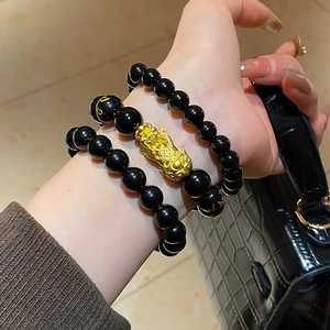 Detailed macro view of black obsidian bead bracelets with gold Pi Xiu charm and engravings