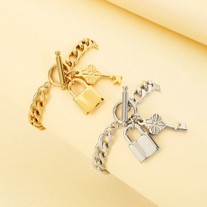 Détail de gourmettes or et argent avec pendentifs clé et cadenas et fermoir à bascule OT