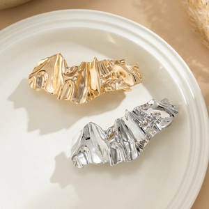 Detailed view of irregular liquid metal hair clips in gold and silver on a ceramic tray