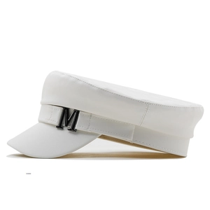 Detail view of the metallic M letter ornament on a white faux leather nautical baker boy hat