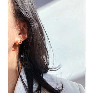 Detail of square gold hoop earrings worn on ear showing sleek geometric metal design