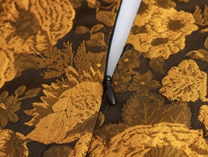 Detailopname van de gouden jacquardstof en de onzichtbare rits op de elegante jurk