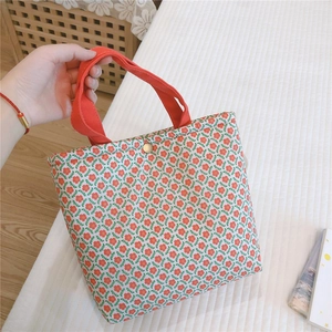 Detail of floral canvas lunch bag showing red strap handle and golden magnetic snap closure