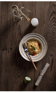 Top-down macro view of beige handmade ceramic pasta bowl on rustic dark wood table