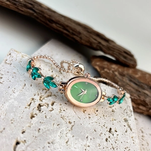 Detail of elegant oval green watch face with leaf-shaped gemstones on rose gold band