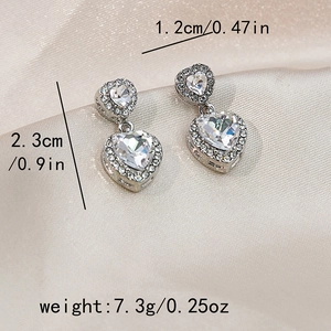 Macro shot of silver heart earrings with white diamonds on satin background