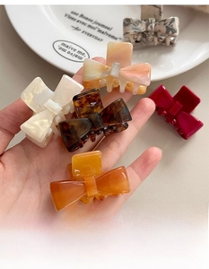 Detail of elegant acetate bow hair claw clip in various colors on decorative white plate