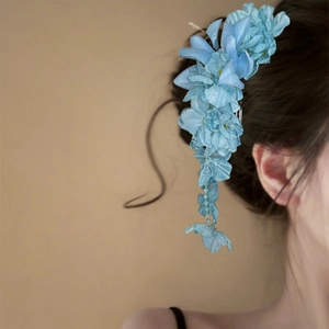 Detailed view of an elegant blue fabric flower hair clip with tassels on model's hair
