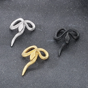 Dettaglio di pendenti a serpente in argento, oro e nero su fondo scuro strutturato