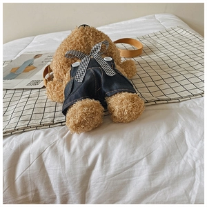 Detail of a brown plush bear bag wearing denim overalls and a checkered bow accessory