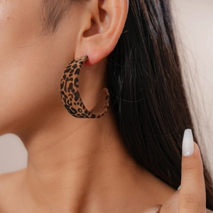 Close-up of a leopard print flocked C-shaped hoop earring worn by a model in detail