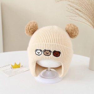 Détail du bonnet en tricot pour bébé avec broderie ours et pompons en fausse fourrure