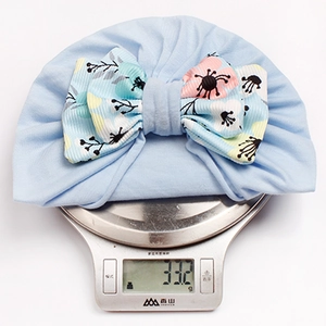 Light blue baby knot beanie with floral bow on a digital scale weighing 33.2 grams