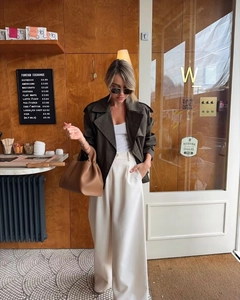 Détail d'un trench court vert olive avec un pantalon large crème et un sac à main en cuir