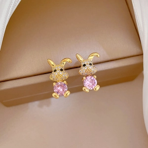 Macro view of gold bunny earrings with pink gemstone and white crystals on silk