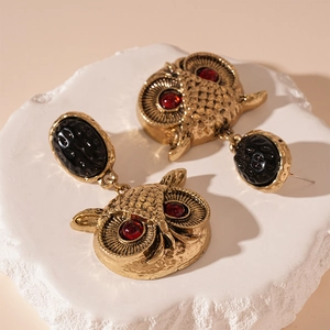 Macro detail of vintage owl earring with black textured oval and red rhinestone eyes