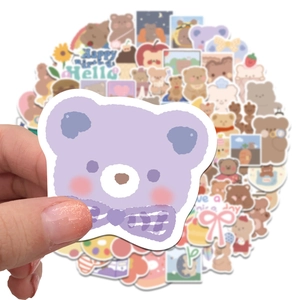 Close-up of a purple cartoon bear sticker held by hand among a pile of cute bear decals