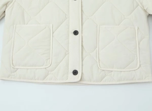 Detail of diamond quilted beige cotton jacket with black button and chest pocket