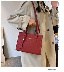 Red quilted leather handbag with heart charm shown on model in beige trench coat