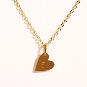 Détail macro du pendentif cœur doré avec gravure de la lettre E sur chaîne fine
