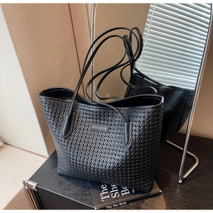 Close-up of black woven leather tote bag with stylish book in a modern lifestyle setting