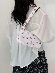 Close-up of white nylon shoulder bag featuring vibrant red cherry patterns on a model