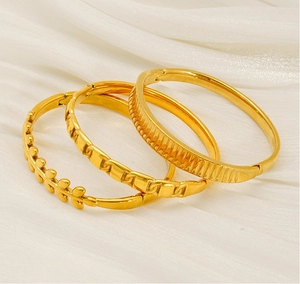 Detail of three gold stainless steel bangles with leaf, chain, and vertical patterns