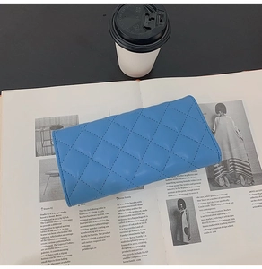 Detailed view of a blue quilted leather long wallet placed on an open art magazine