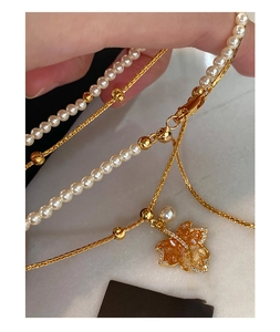 Detail of double-layer necklace featuring amber maple leaf pendant and white pearl beads