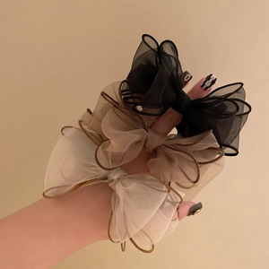 Three organza scrunchies in black, brown and beige held against a neutral background