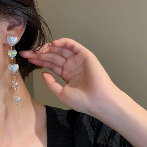 Close-up of golden tassel earrings with heart-shaped pearls and crystals on a model