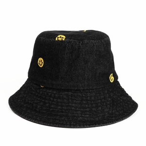 Close-up of yellow smiley face embroidery on black denim bucket hat texture