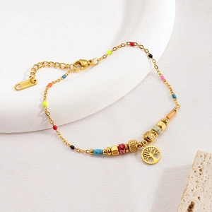 Macro shot of stainless steel tree of life charm with colorful beads on a gold bracelet