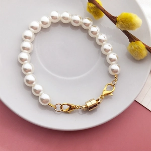 Detailed close-up of a white pearl bracelet with a golden magnetic clasp and lobster claw hook