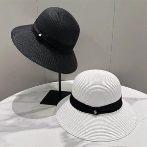 Close-up of woven straw hats featuring black ribbons and elegant gold charms