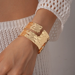 Macro detail of wide gold cuff bracelet featuring irregular hammered texture and cutouts