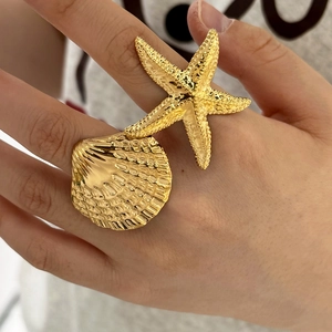 Detail of a large gold starfish and seashell adjustable ring worn on a hand