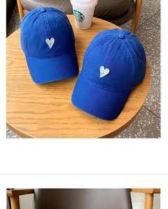 Detail of navy blue baseball caps with white heart embroidery on a wooden table