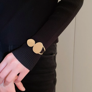 Close-up of golden irregular double-disc cuff bracelet on a black knit sleeve