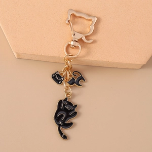 Detailed view of golden keychain featuring three cute black cat pendants on a beige mat