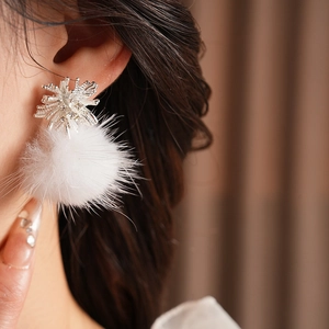 Detail view of silver zircon snowflake earrings with white plush pom-poms on ear